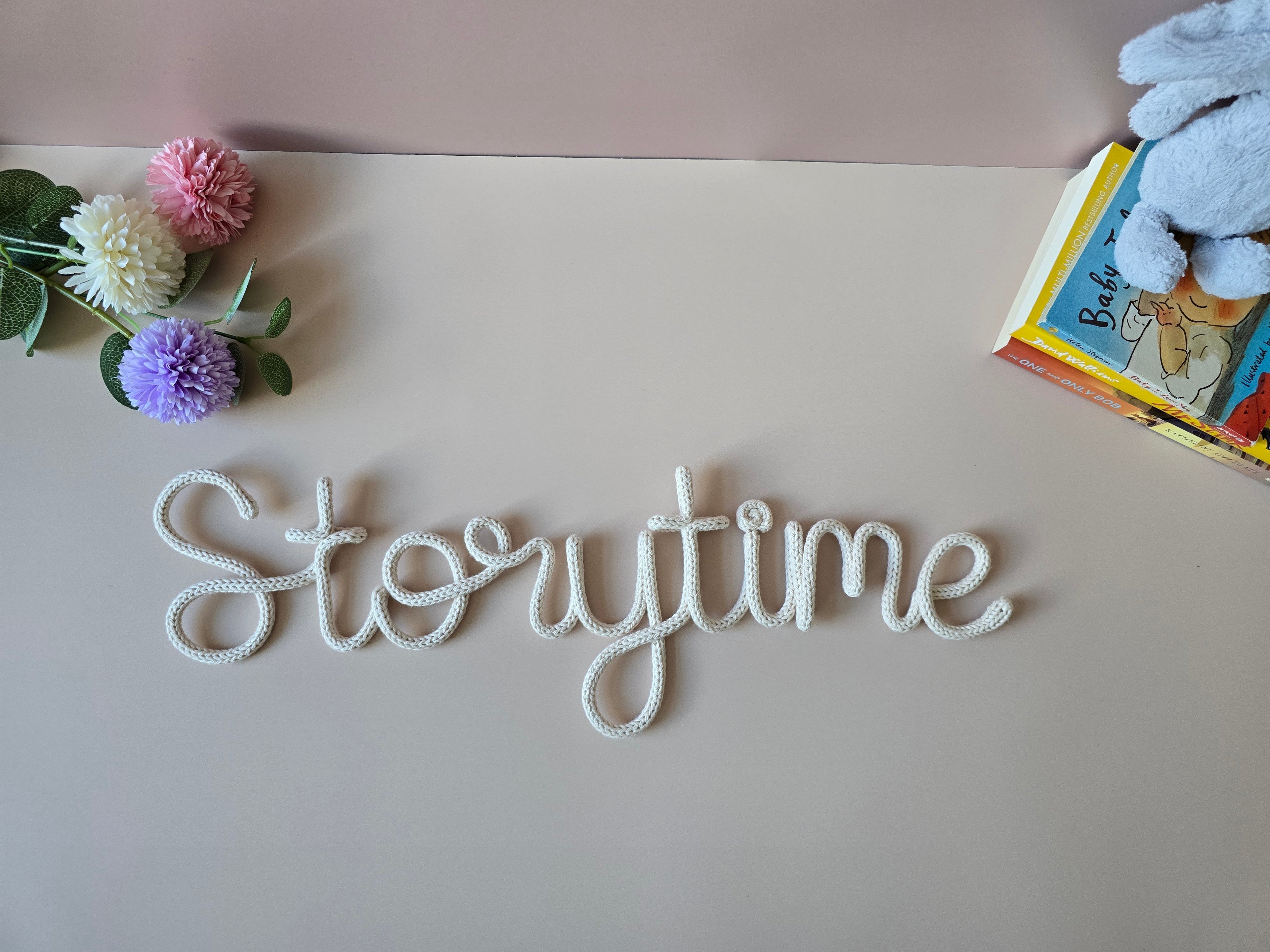 Decorative word 'Storytime' on a surface with flowers and a book in the background.