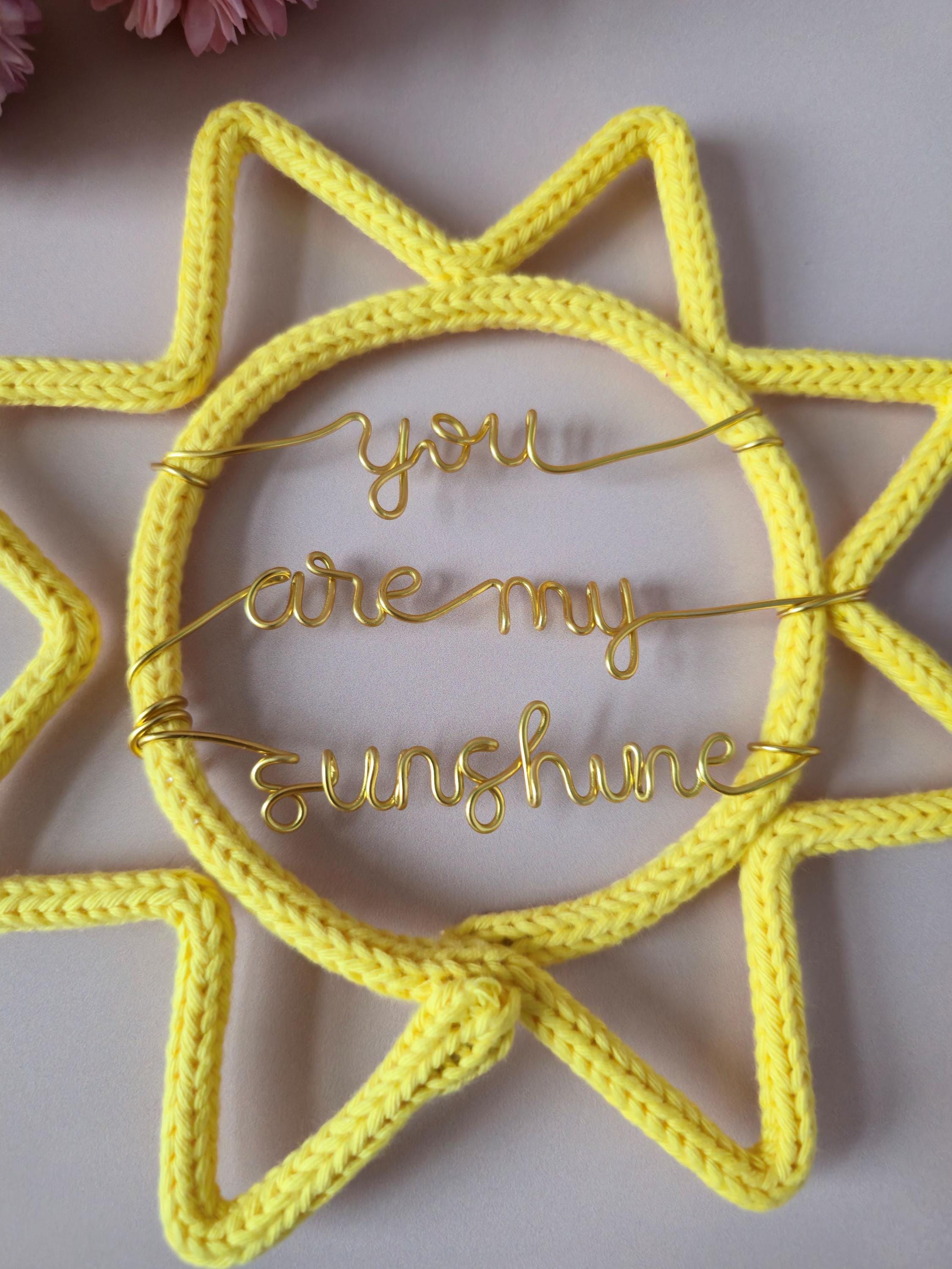Yellow sun-shaped decoration with 'you are my sunshine' text on a light pink background