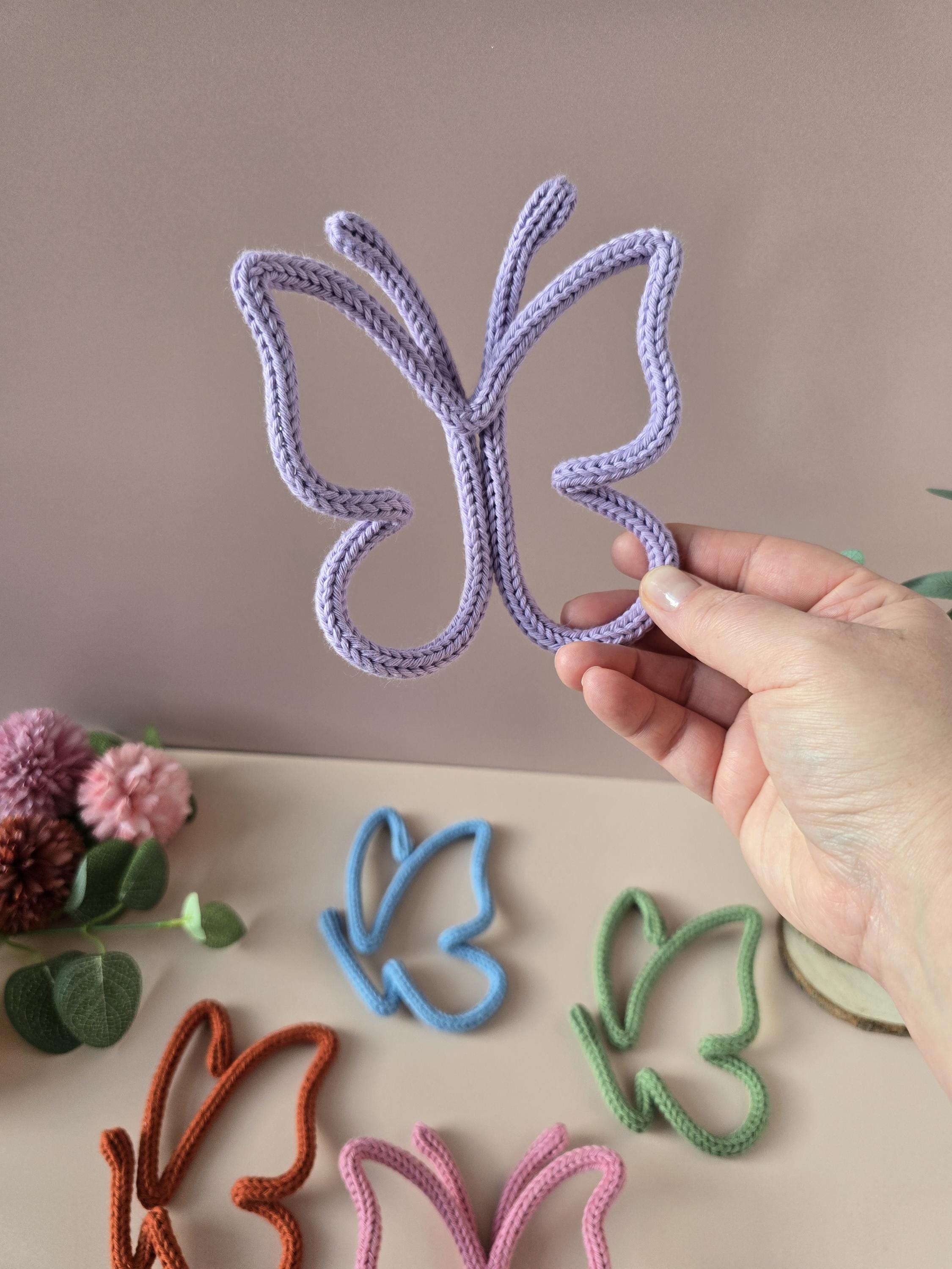 Hand holding a purple butterfly-shaped object with other colorful butterflies on a neutral background