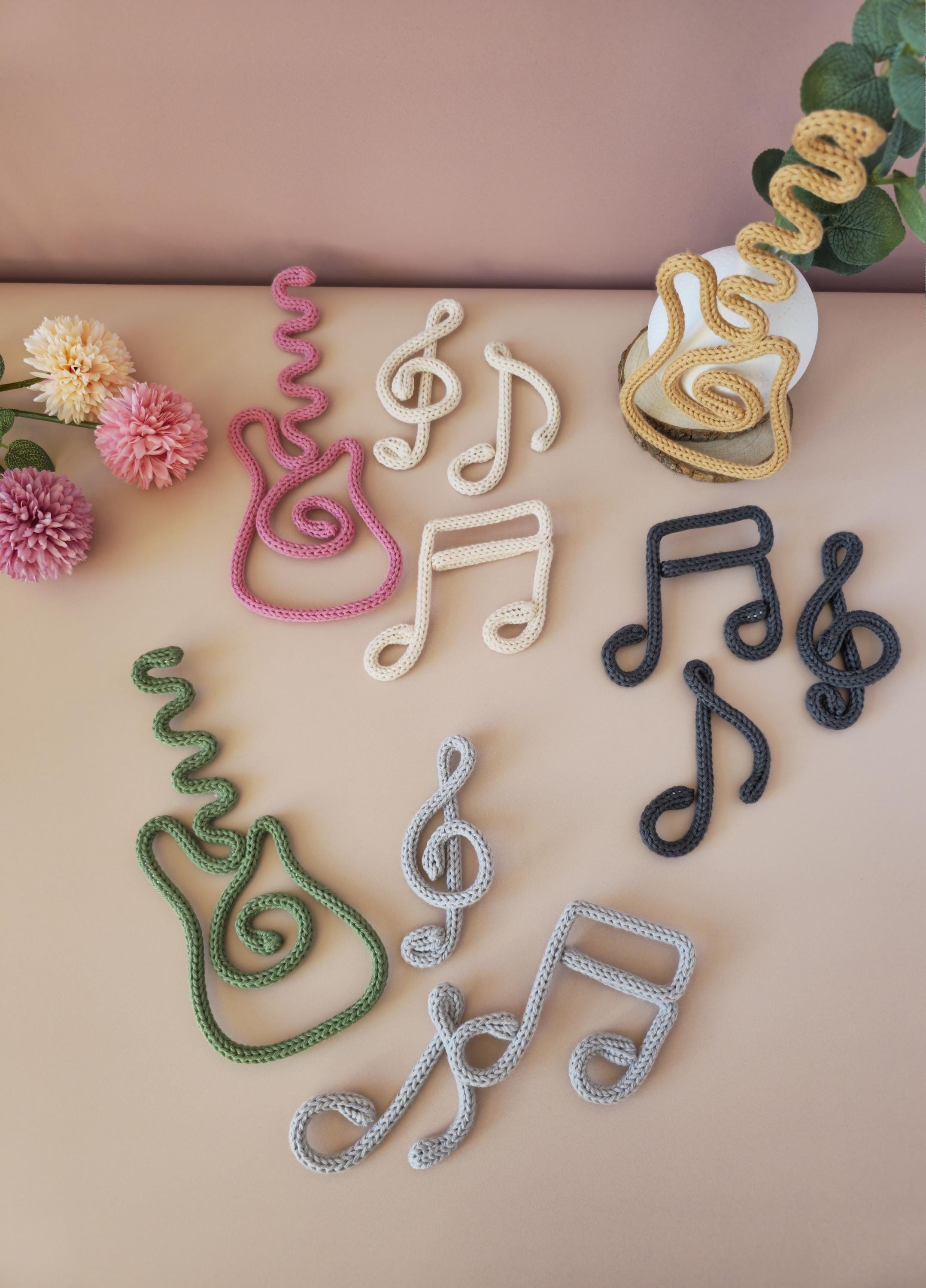 Decorative music notes and treble clefs made of yarn on a beige surface with flowers and leaves.