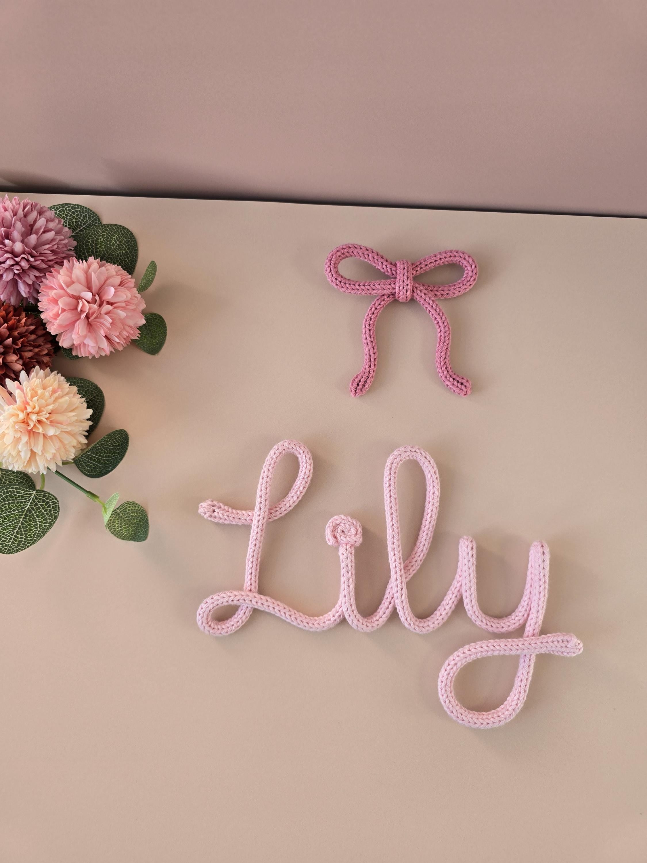 Pink decorative word 'Lilly' and bow on a beige background with flowers.