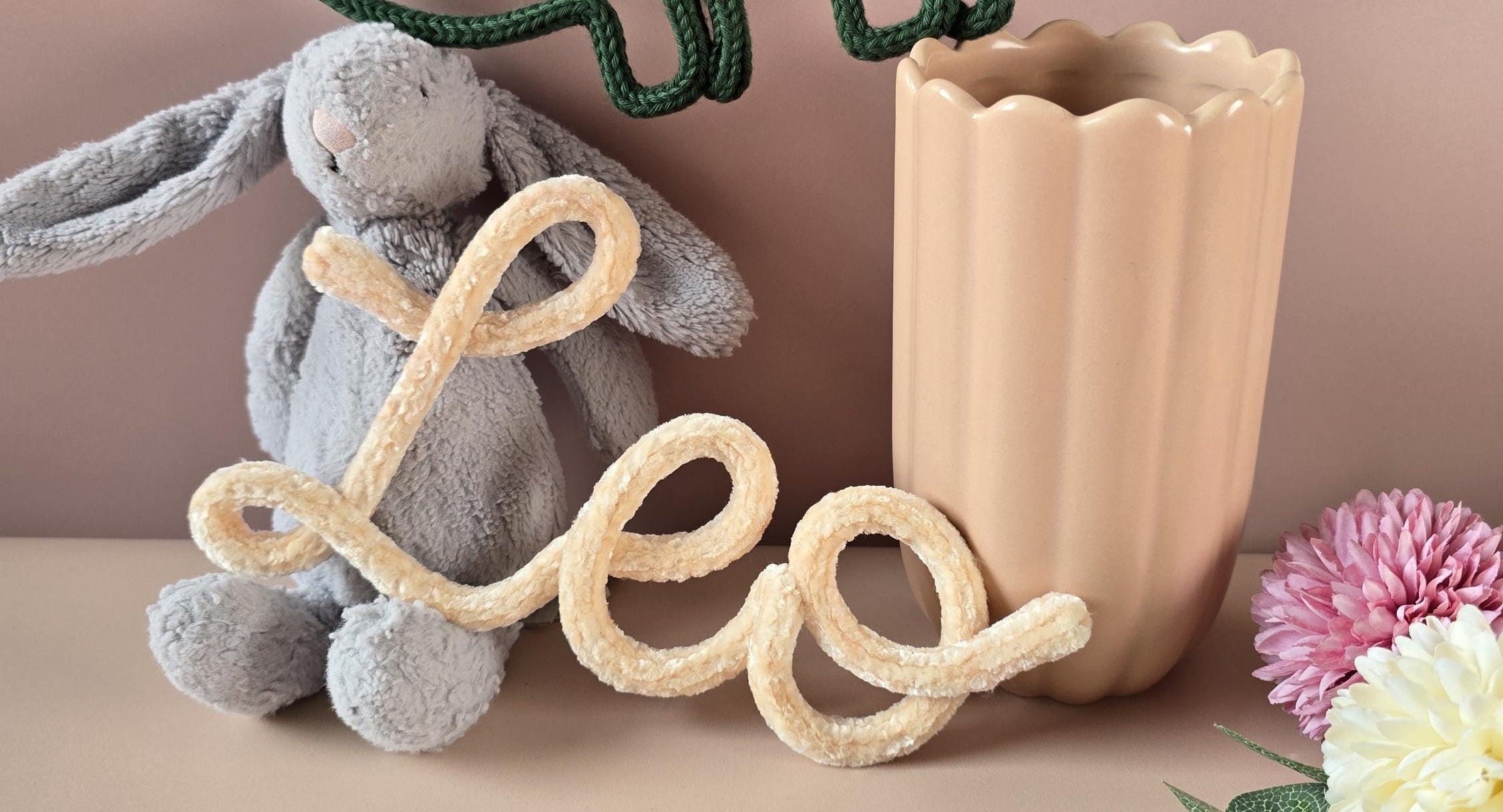 Decorative letter 'L' with a plush rabbit toy and vase on a beige background