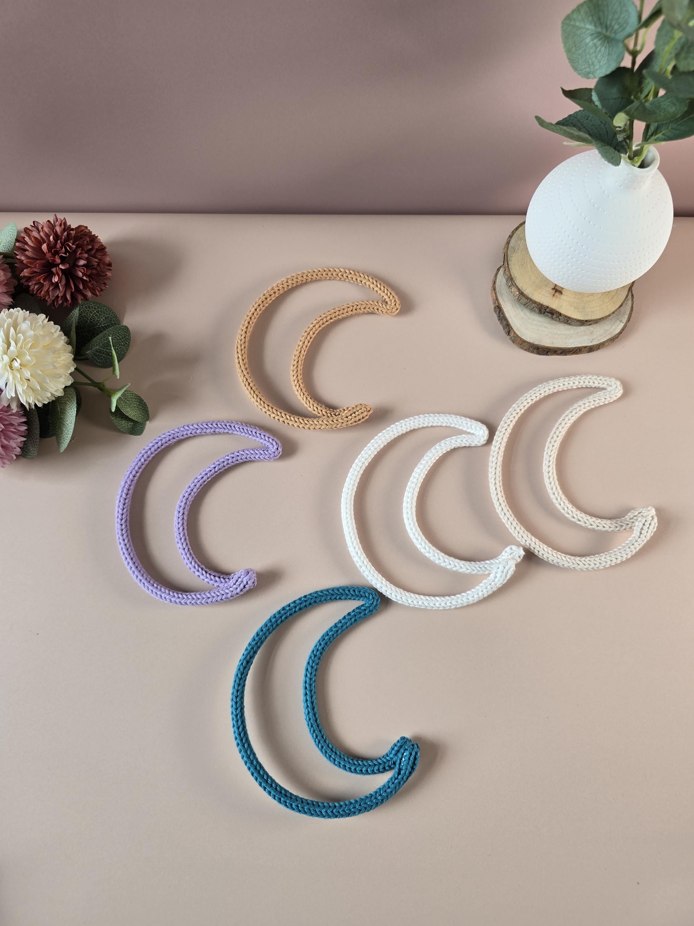 Decorative moon-shaped coasters in various colors on a beige surface with flowers and a plant.