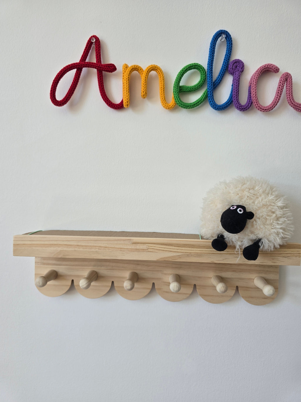 Rainbow personalised name sign reading Amelia displayed on a children’s bedroom wall above a wooden shelf.