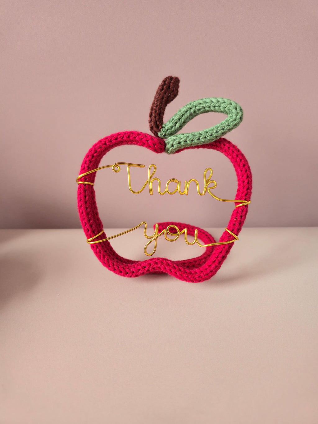 Crocheted apple-shaped sign with 'Thank you' text on a pink background