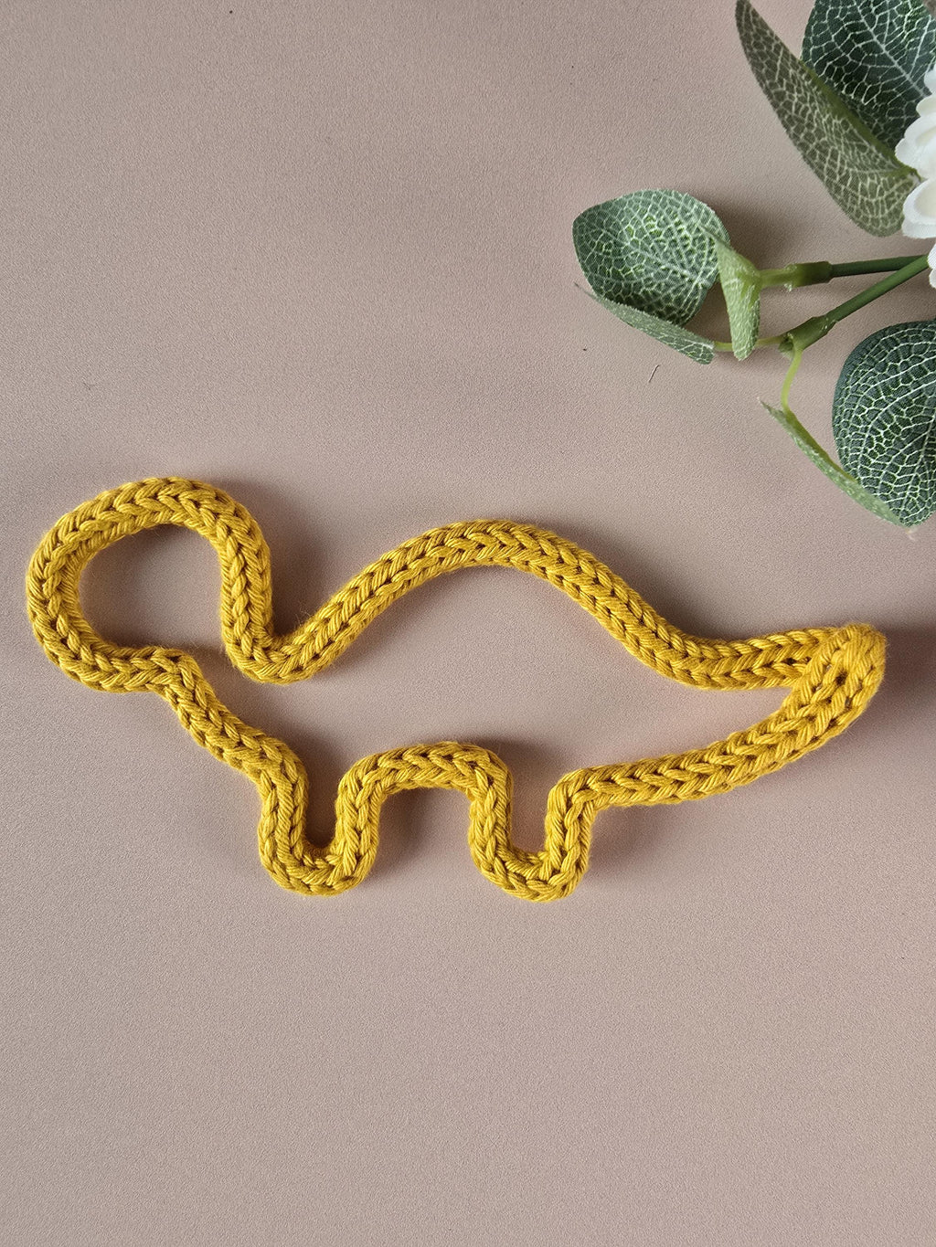 Yellow knitted dinosaur toy on a beige background with green leaves.