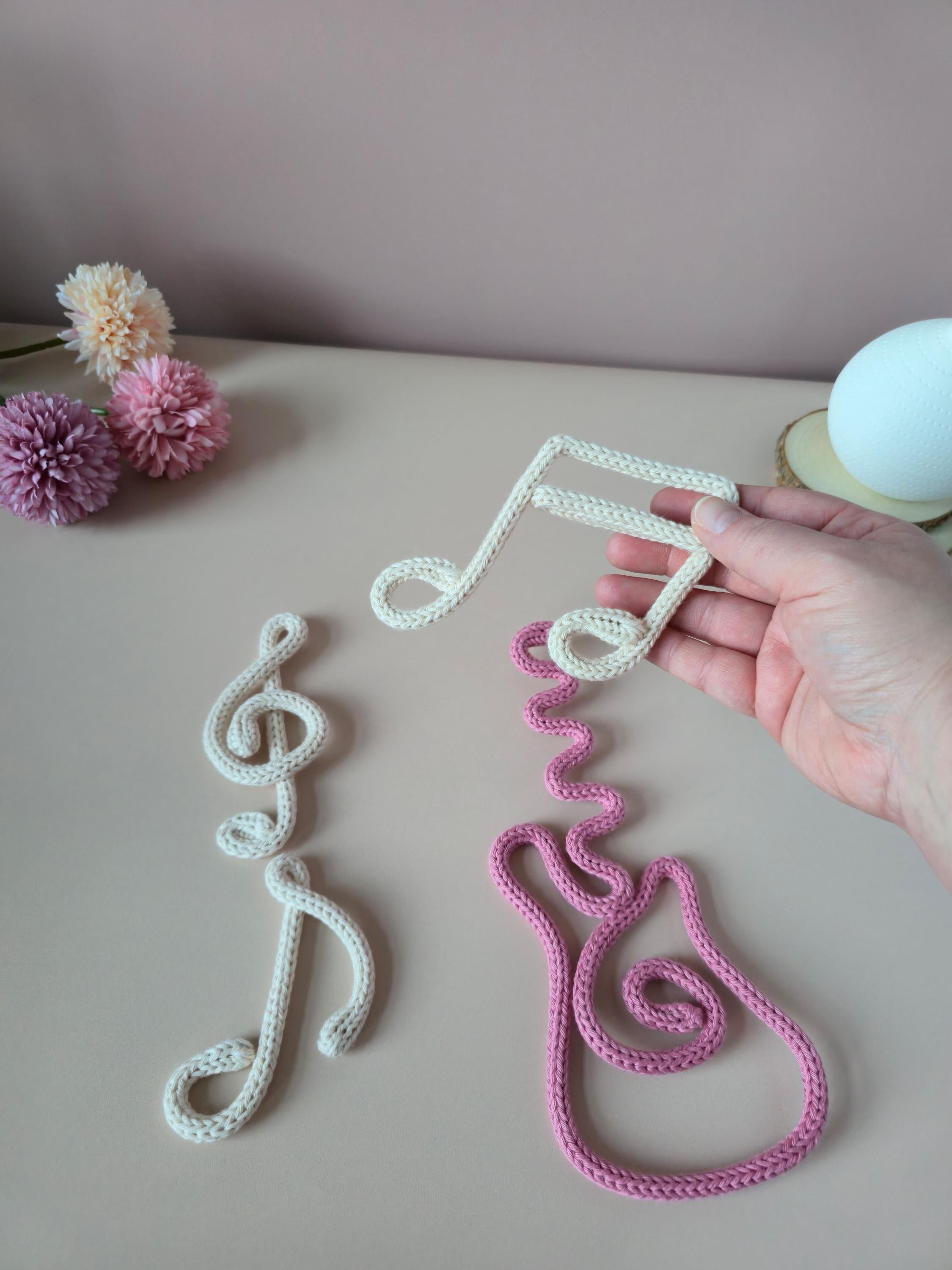 Handmade crochet music note decorations on a table with flowers in the background.