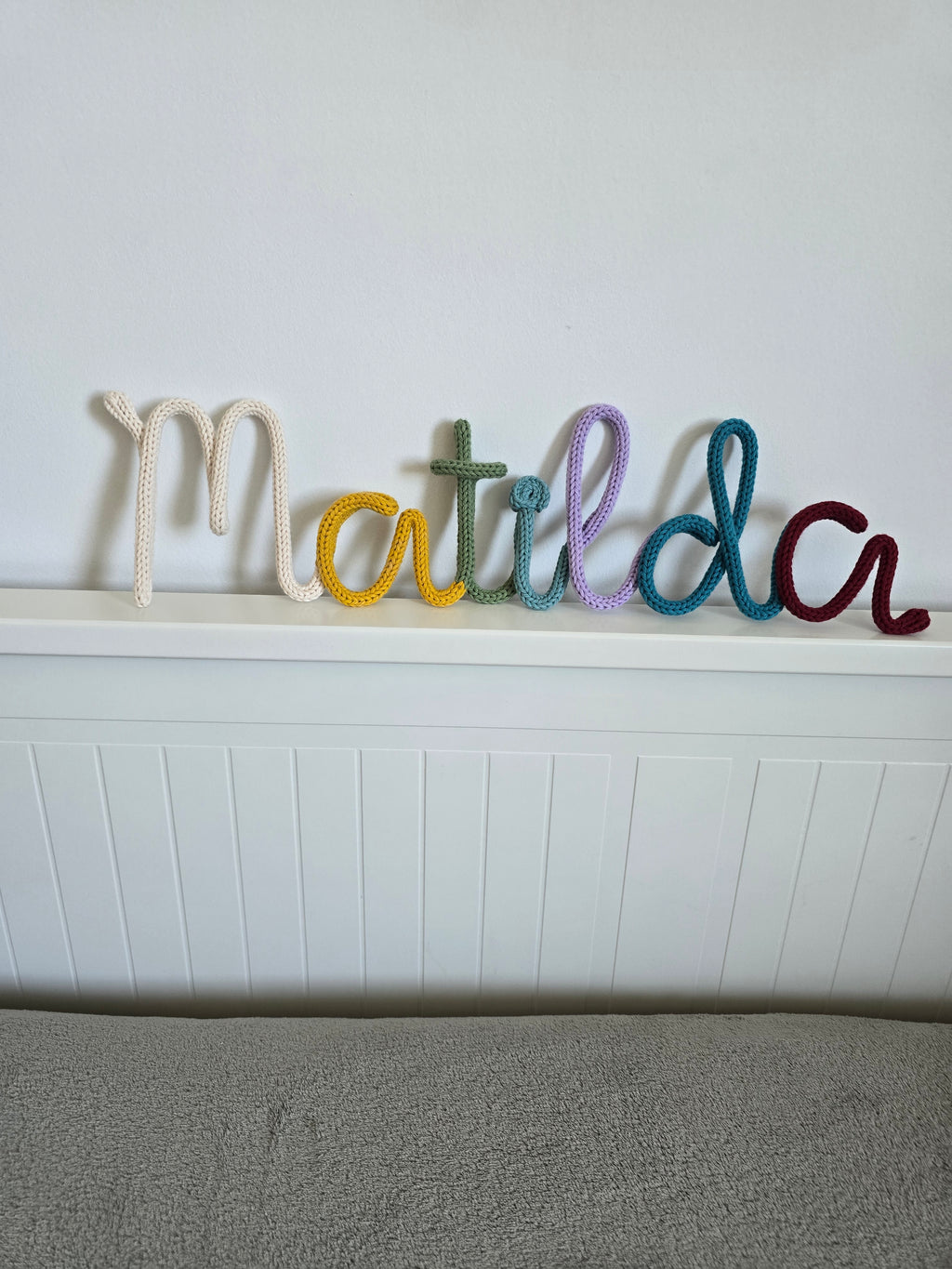 Close-up of a multicoloured personalised knitted wire name sign reading Matilda, showing the CraftyBabs signature colour mix in soft cotton yarn.