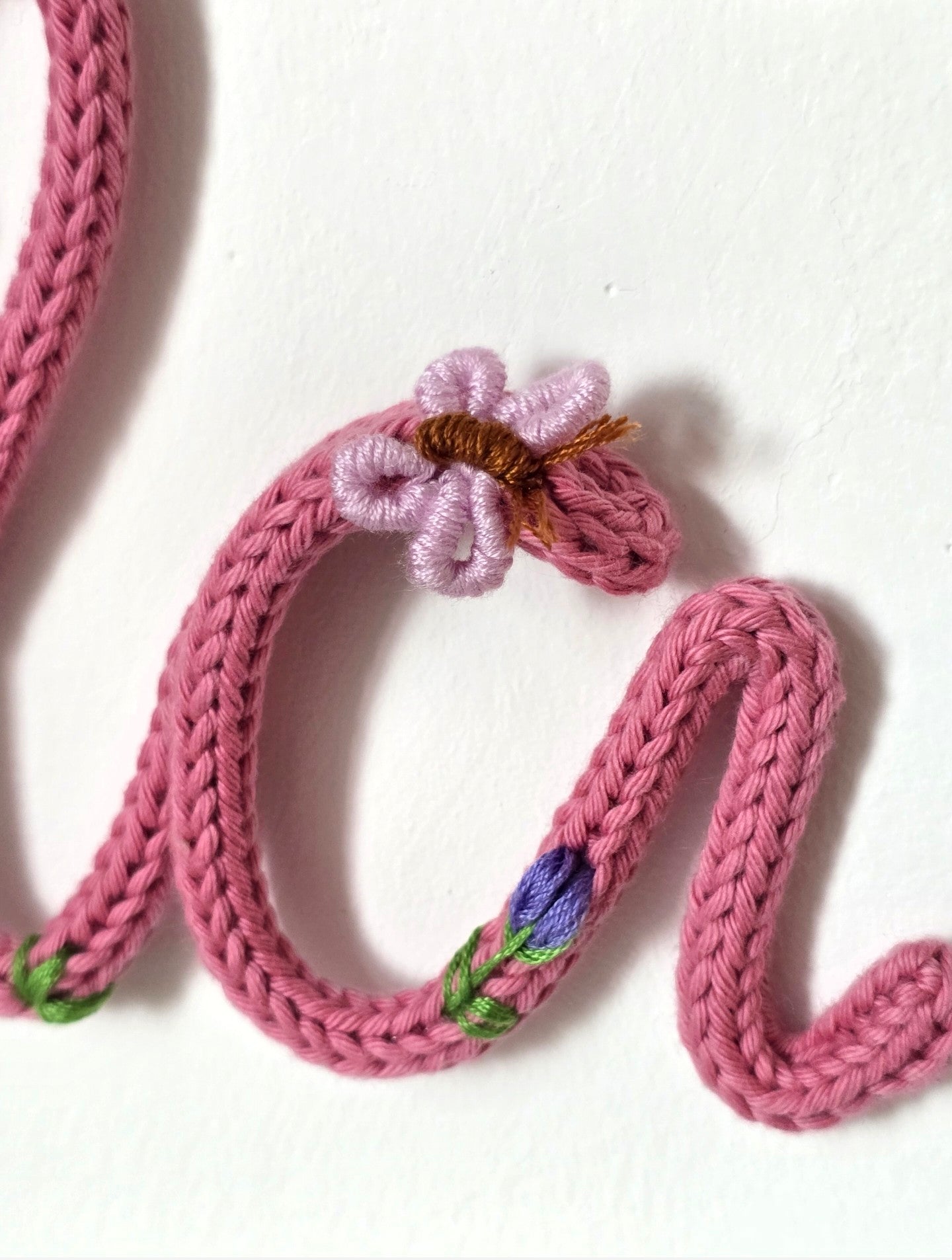 Close-up of hand-embroidered flowers on the pink knitted wire name sign Ela