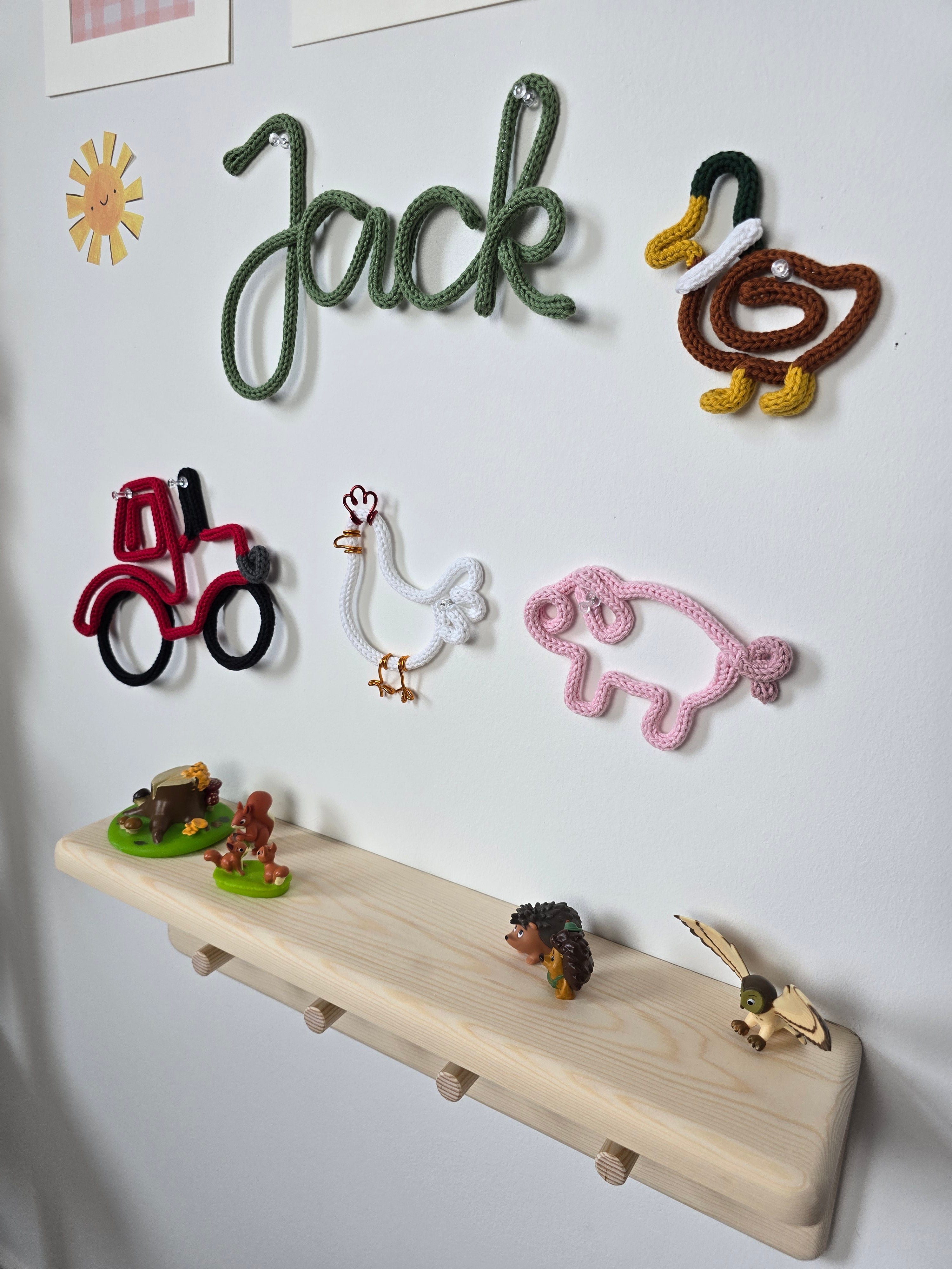 Close-up of a handmade knitted wire tractor and chicken displayed on a children’s bedroom wall.