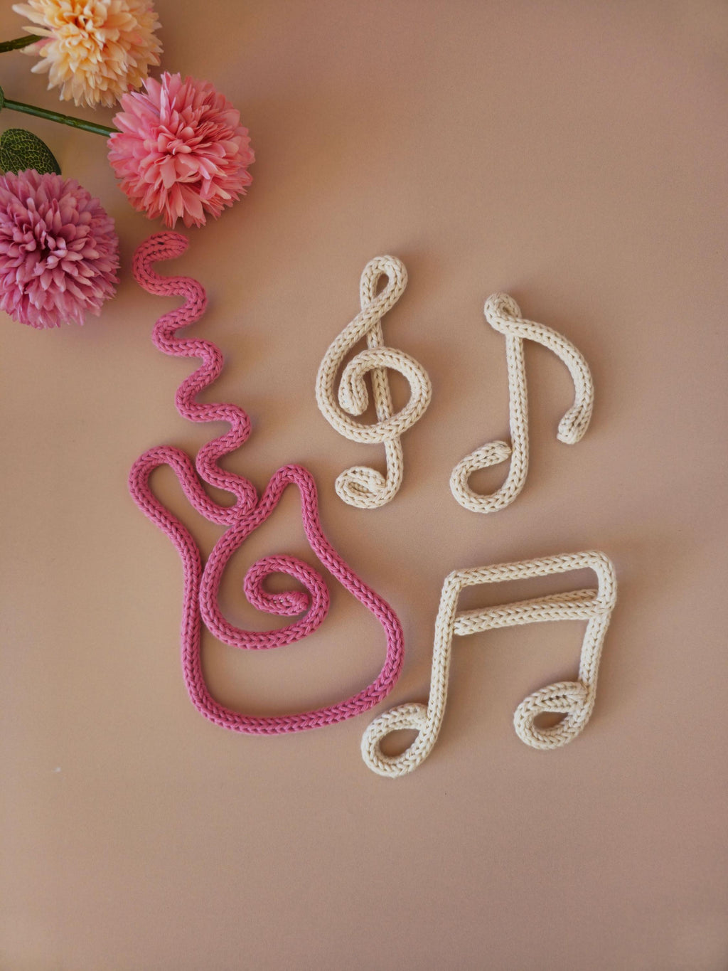 Close-up of handmade knitted wire music decor shapes including guitar, treble clef and musical notes in soft cotton yarn.