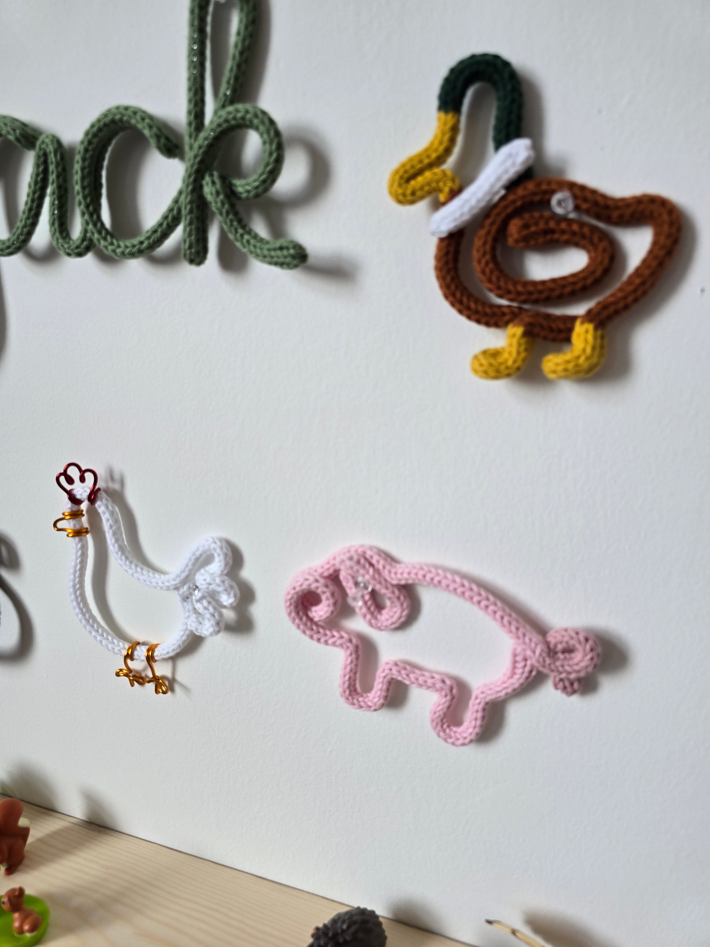 Handmade knitted wire duck and pink pig farmyard wall decorations in a child’s room.