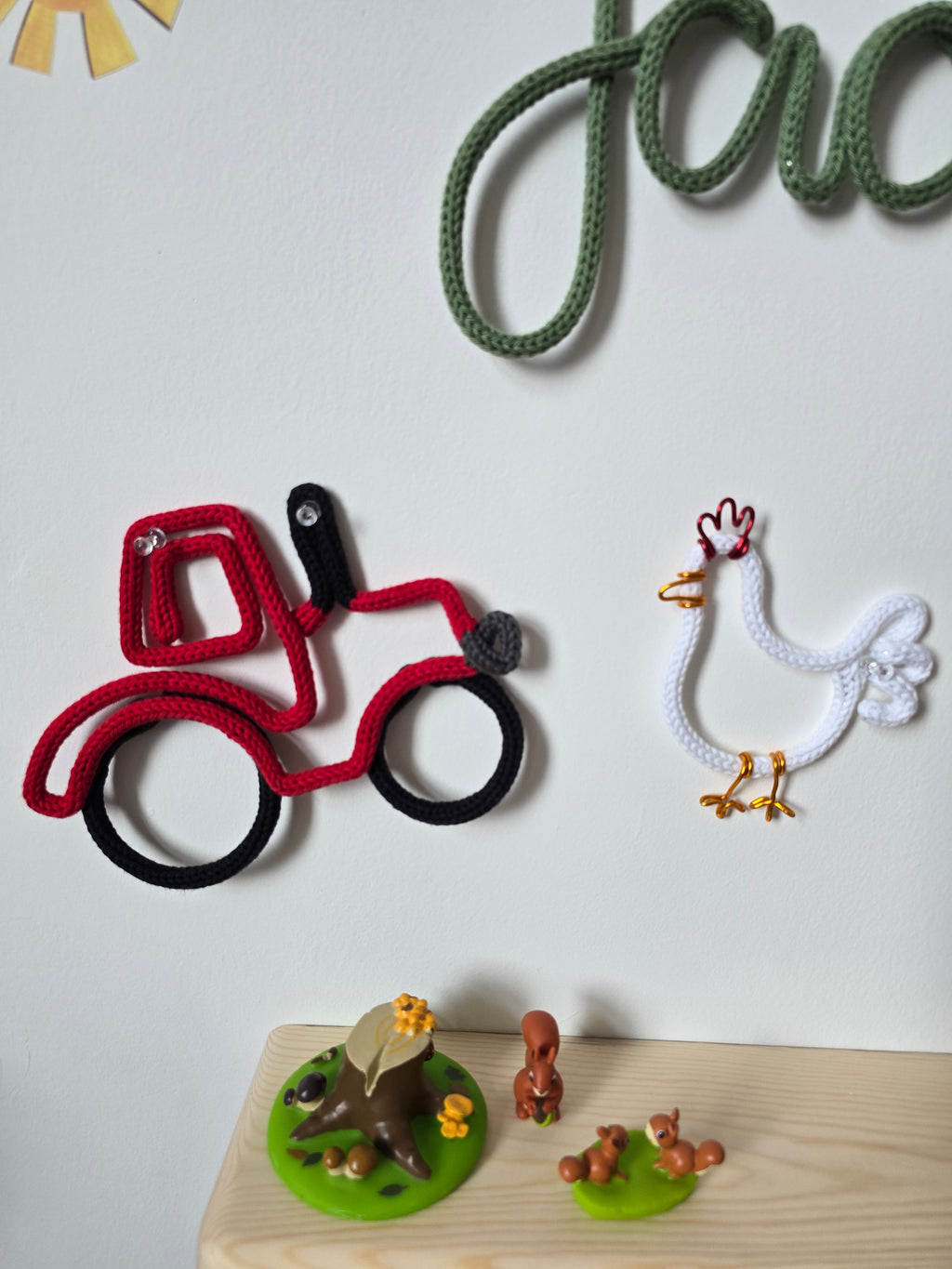 Red knitted wire tractor and white chicken wall decorations above a wooden children’s shelf.
