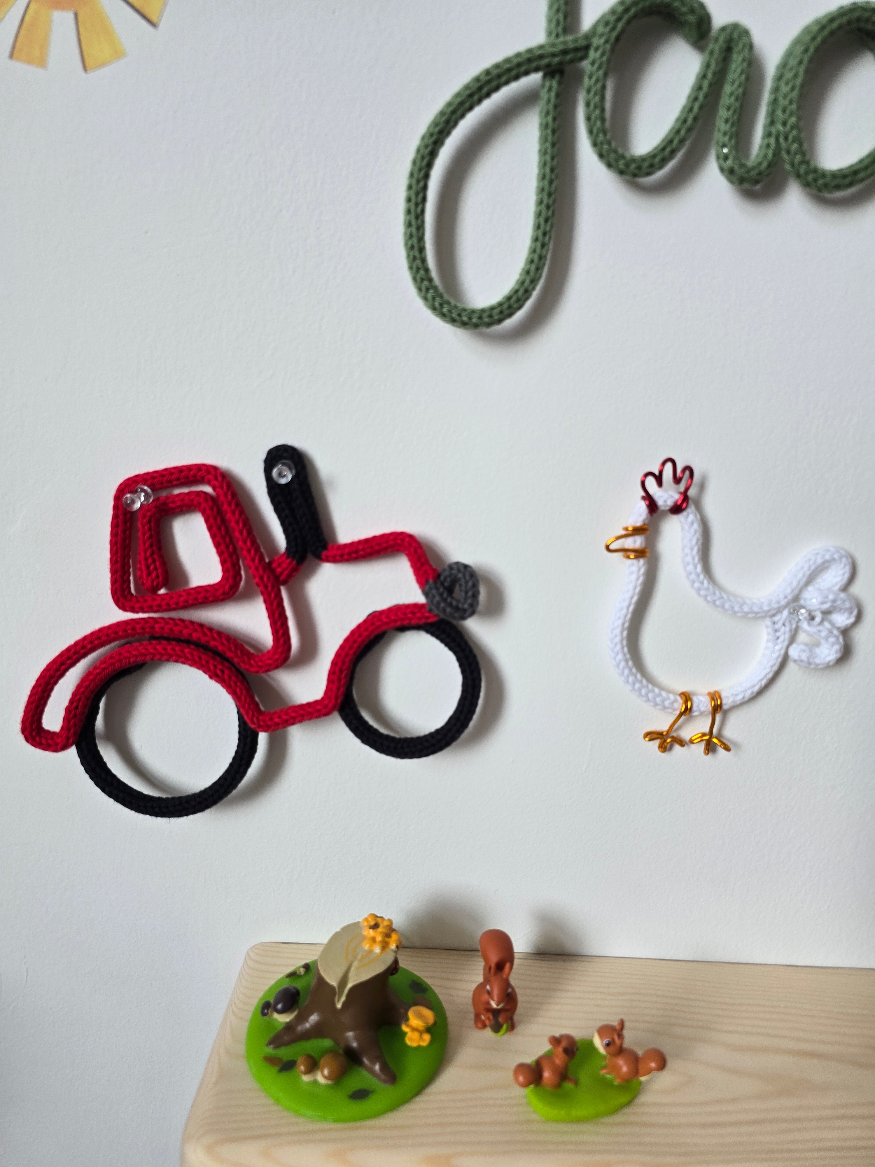 Red knitted wire tractor and white chicken wall decorations above a wooden children’s shelf.