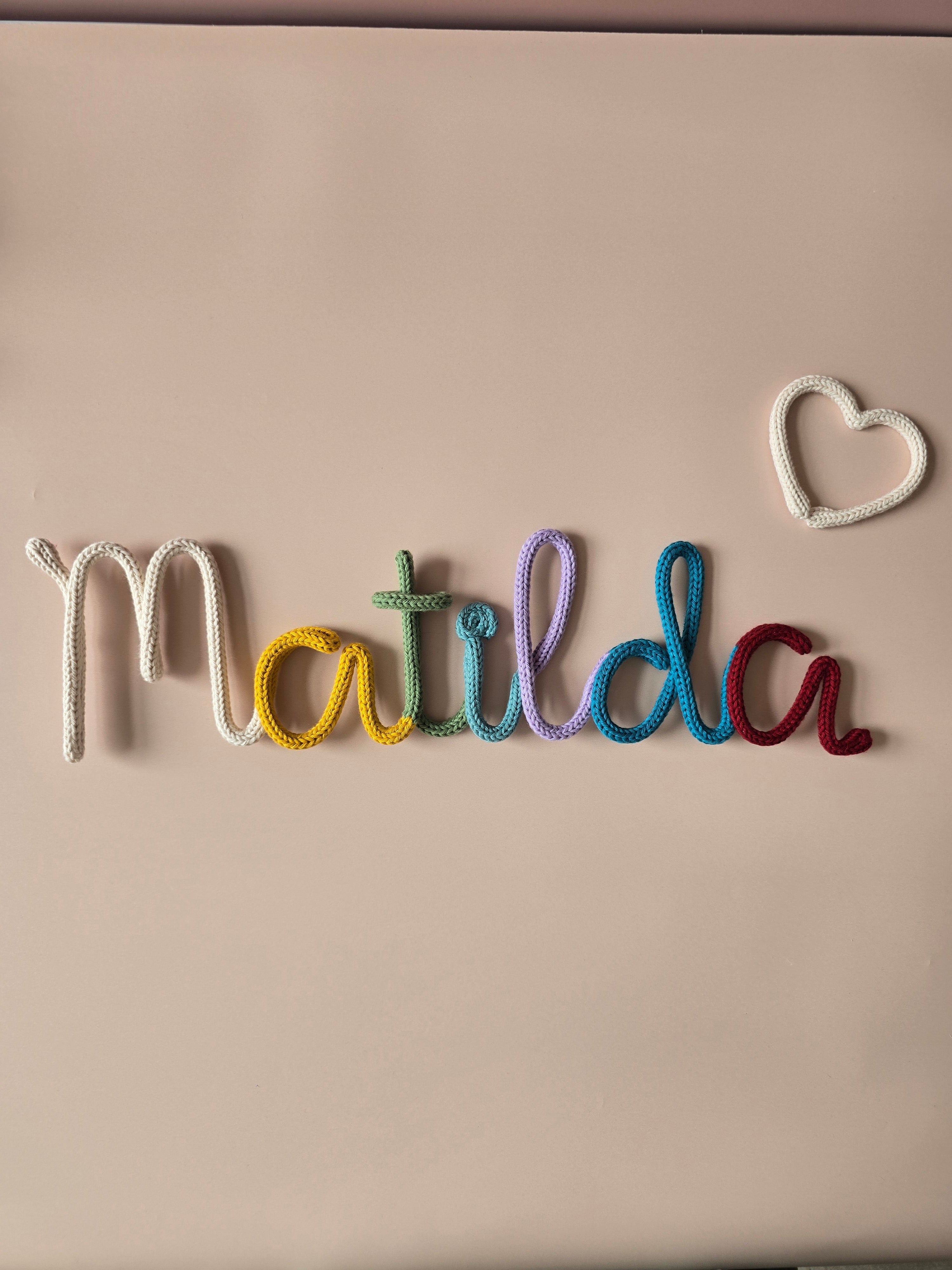 CraftyBabs multicoloured knitted wire name sign with a small heart detail, handmade for nurseries and children’s bedrooms.
