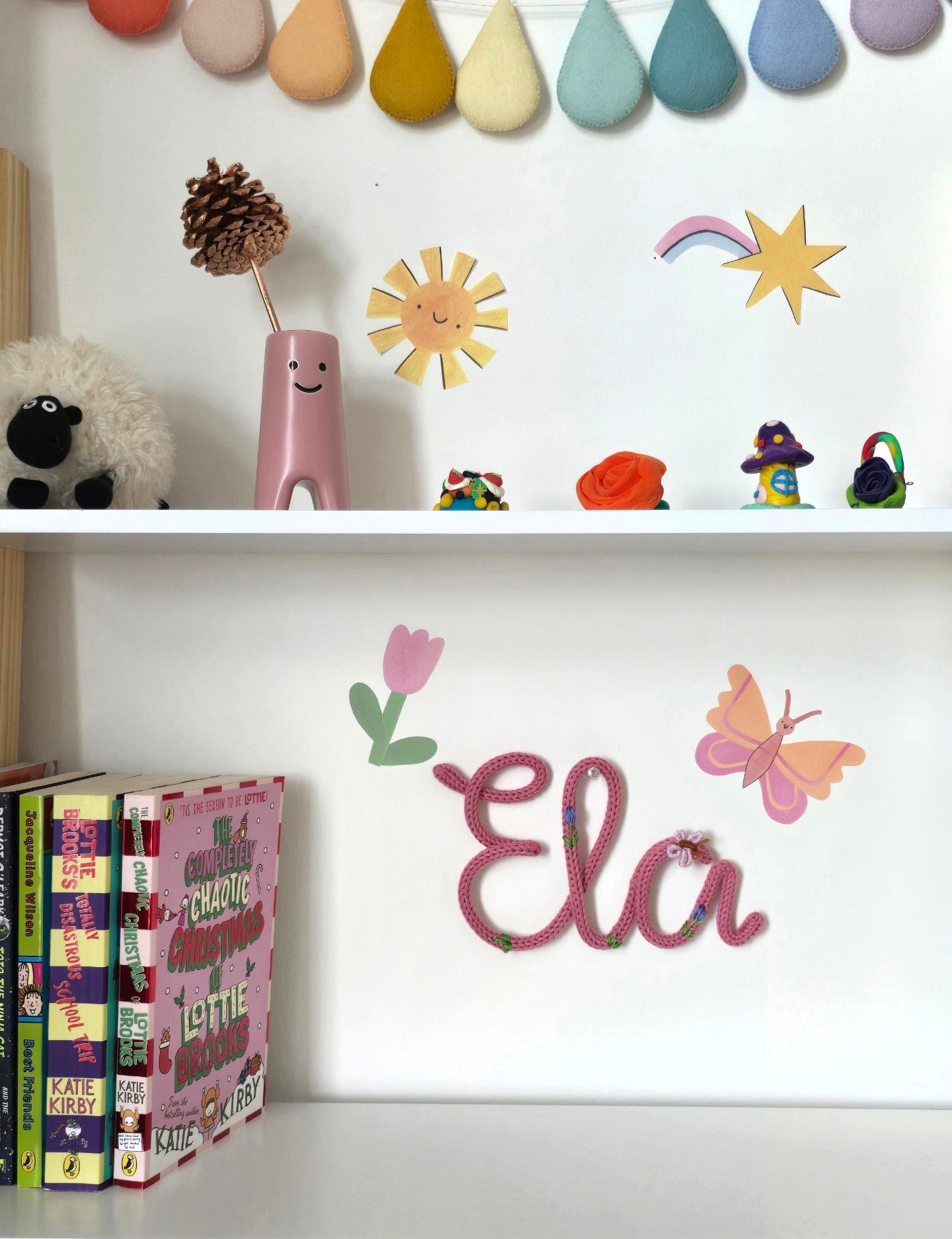 Pink Ela embroidered knitted wire name sign in Butterfly Bloom style on a children's bedroom wall.