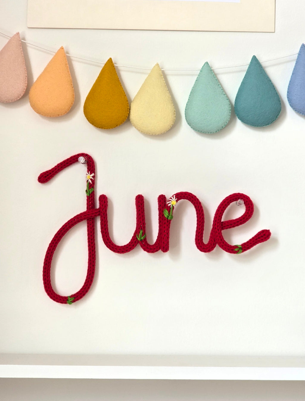 Personalised embroidered knitted wire name sign June in Meadow style on children's bedroom wall.