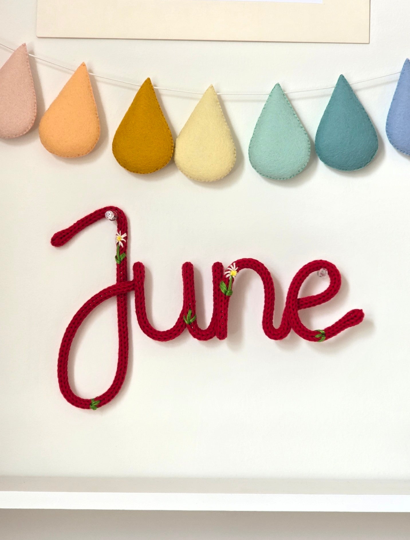Personalised embroidered knitted wire name sign June in Meadow style on children's bedroom wall.