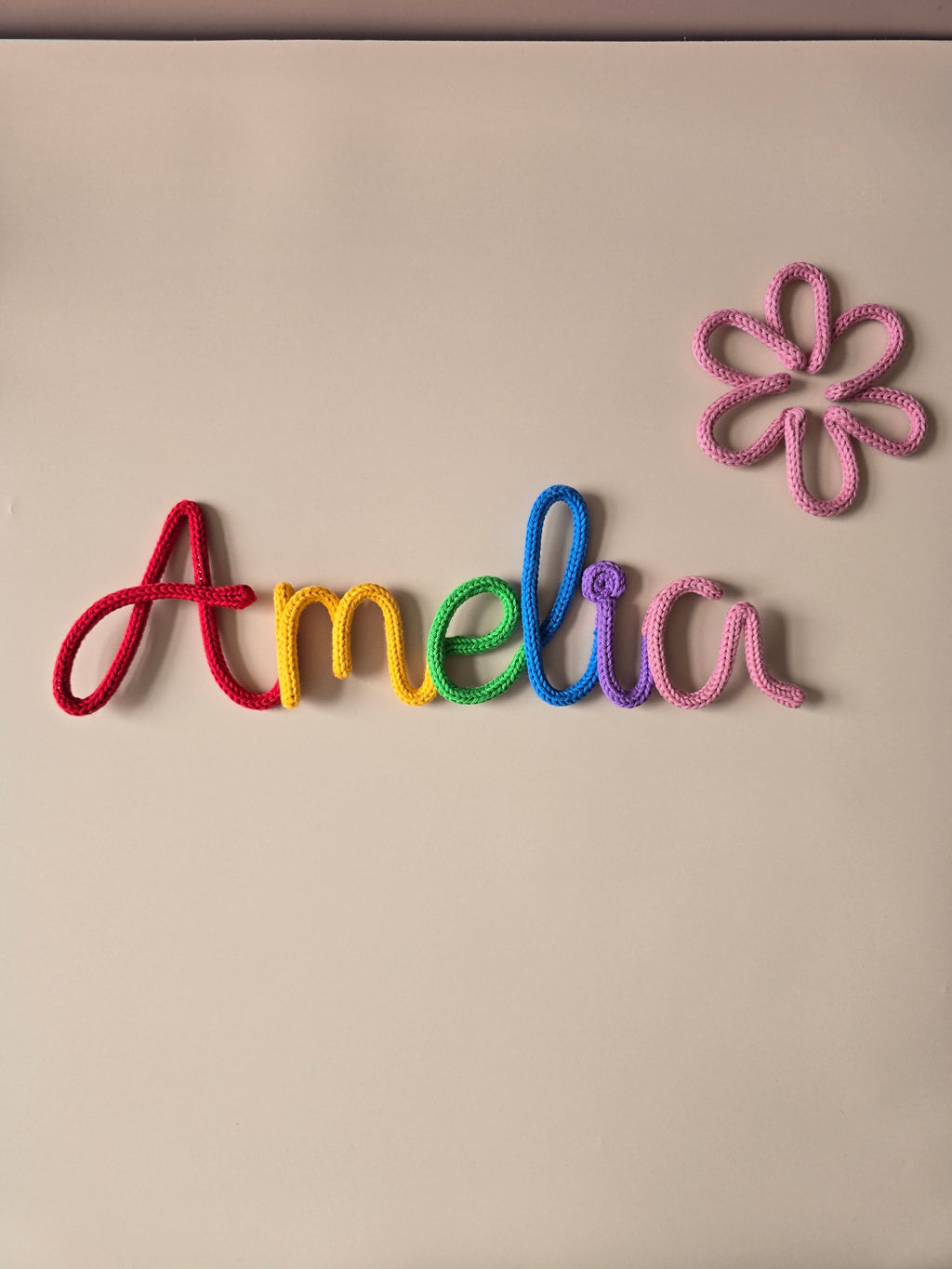 Rainbow personalised knitted wire name sign reading Amelia with a pink flower detail, handmade for children’s room decor.