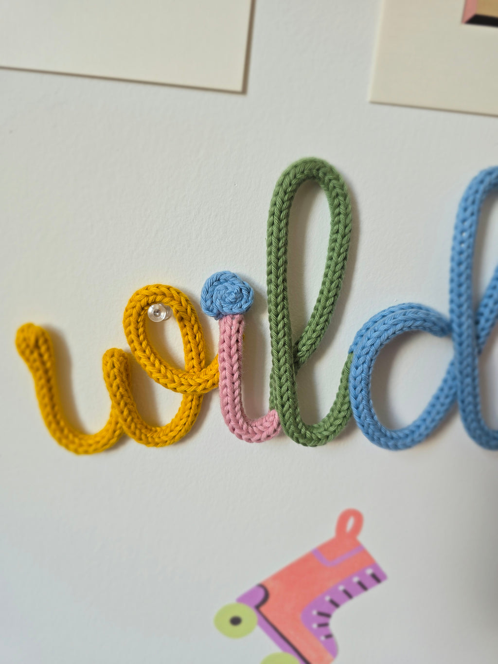 Detailed view of the mustard, pink, green and blue letters in the Wildflower knitted-wire wall word.