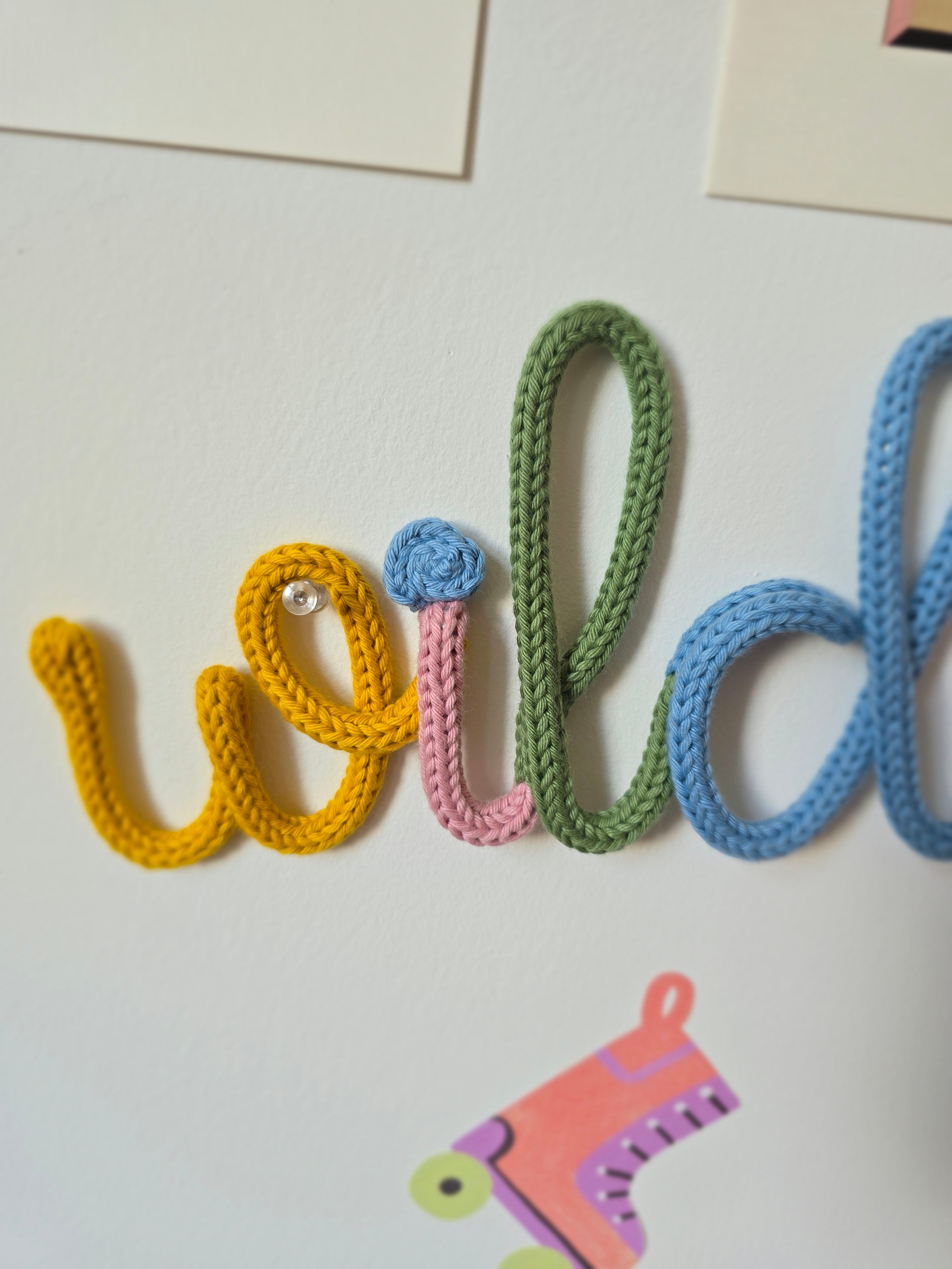 Detailed view of the mustard, pink, green and blue letters in the Wildflower knitted-wire wall word.