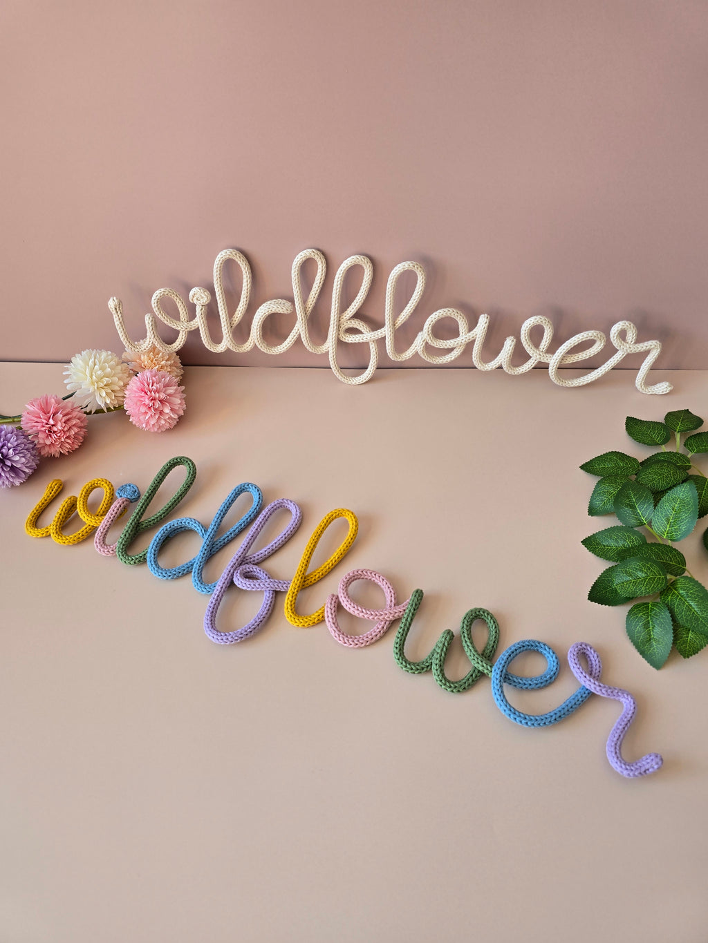 Cream and multicolour Wildflower knitted-wire wall words displayed together with flowers and greenery.